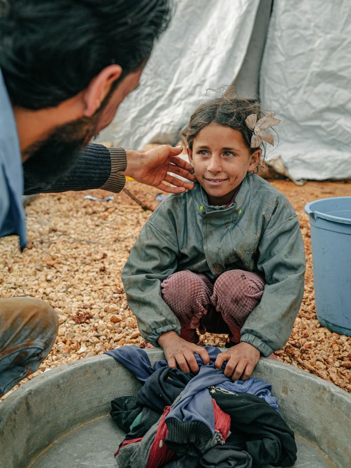 A young girl at a refugee camp in Idlib, Syria, smiling warmly while sitting by a basin.