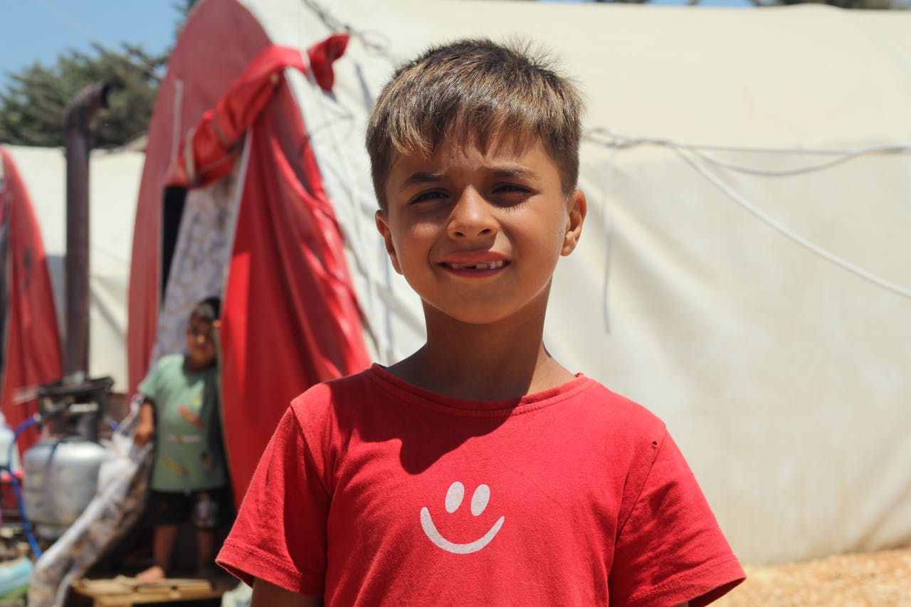 A young boy smiles in a refugee camp, portraying hope and resilience.
