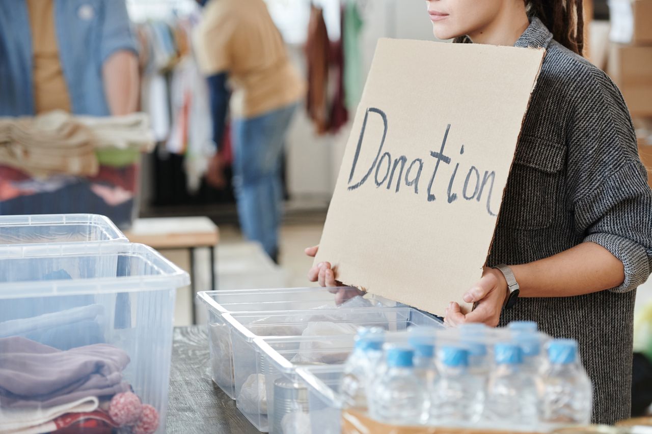 A volunteer holds a cardboard donation sign at a charity event with donation boxes ready for collection.